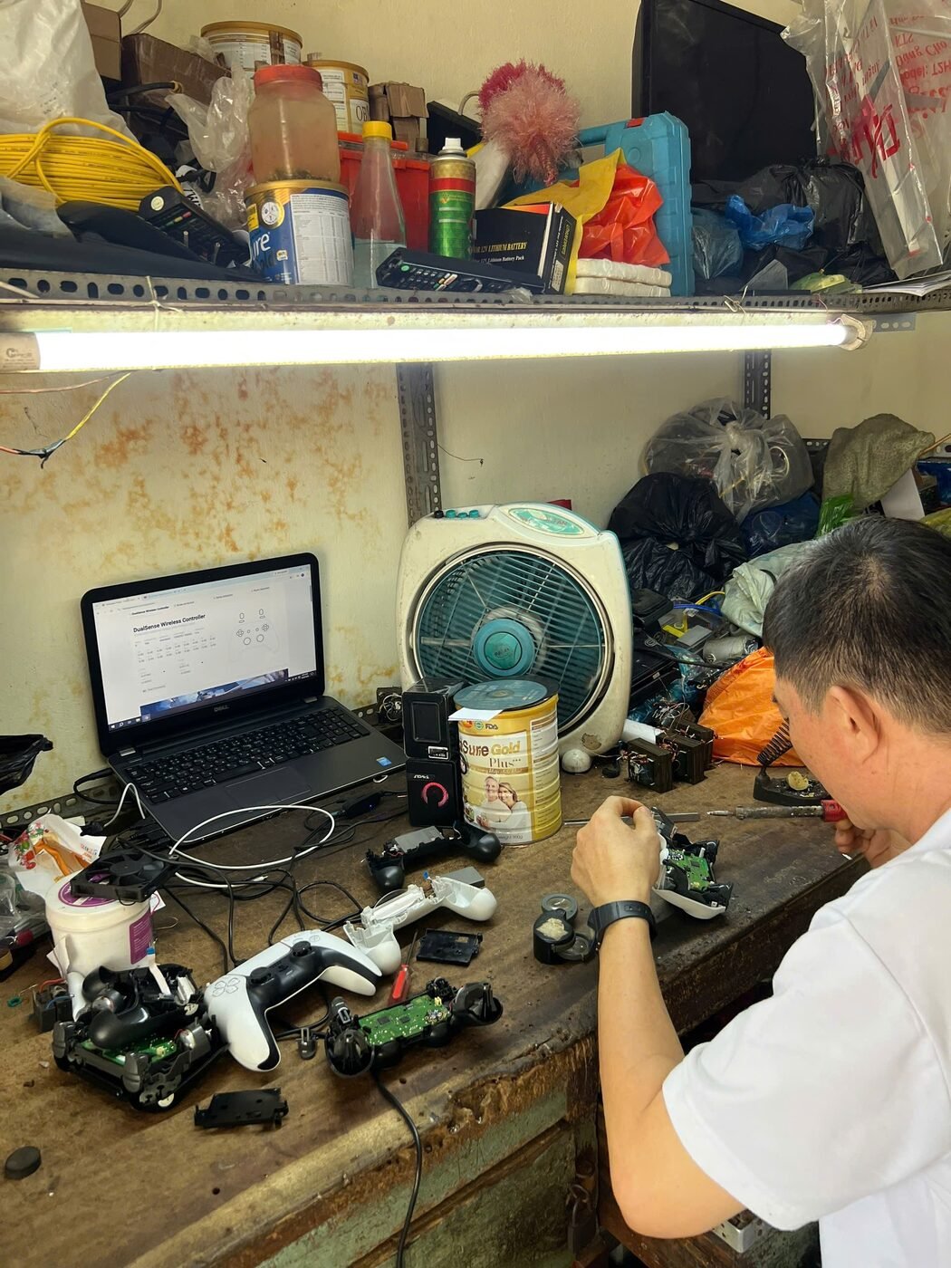 Thợ đang sửa tay cầm PS5 DualSense tại bàn kỹ thuật, màn hình laptop hiển thị phần mềm test nút và cần analog
