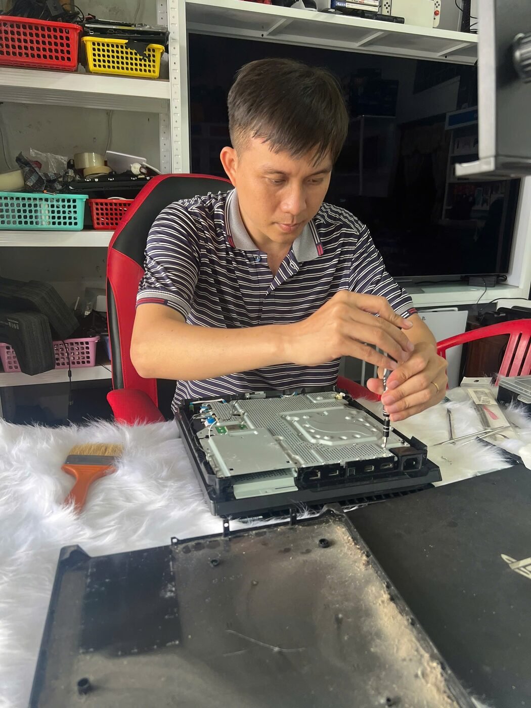 Kỹ thuật viên tháo máy PS4 bằng tua vít để vệ sinh quạt và thay keo tản nhiệt, nắp máy bám đầy bụi